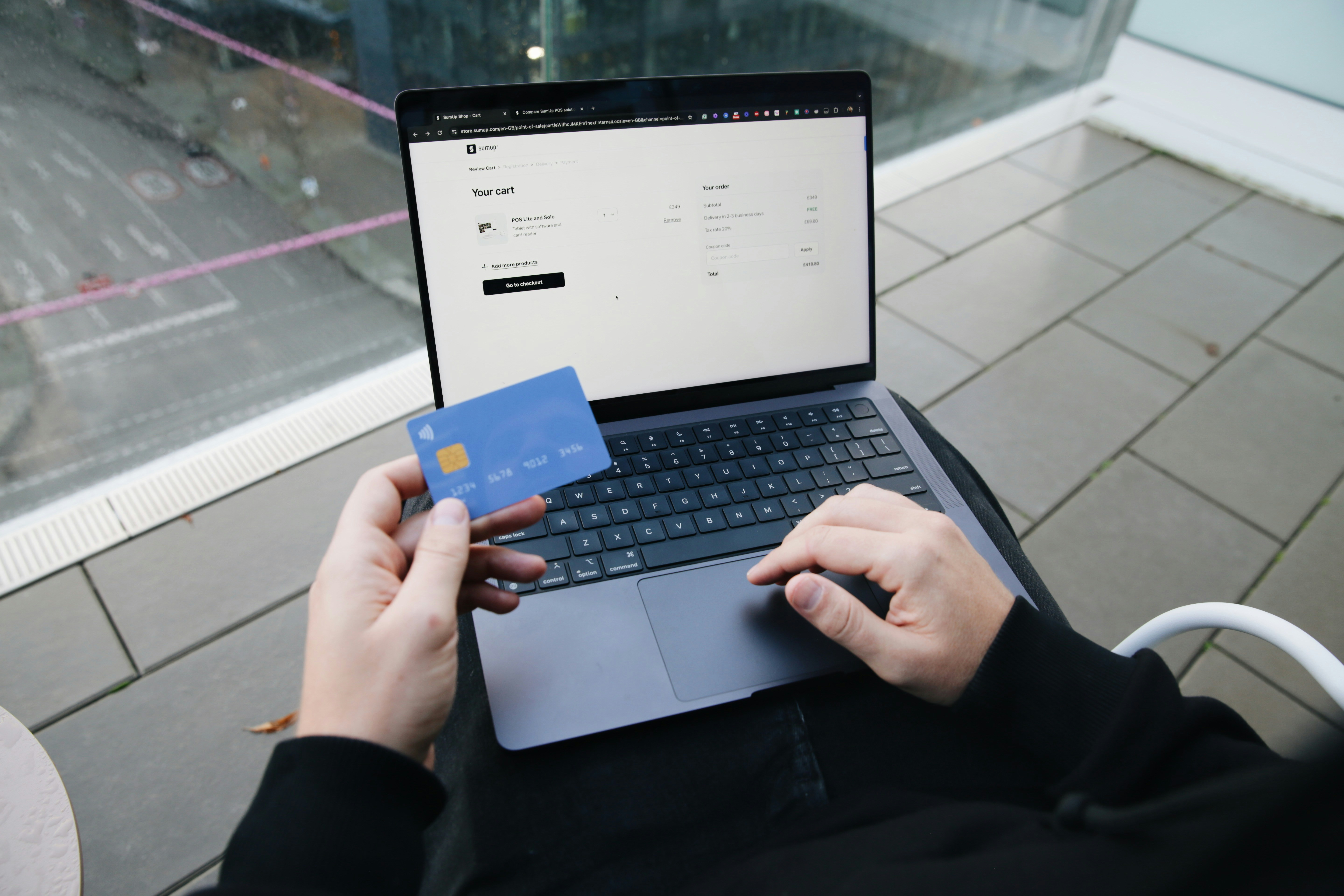 Person holding a blue payment card while using a laptop for an online purchase